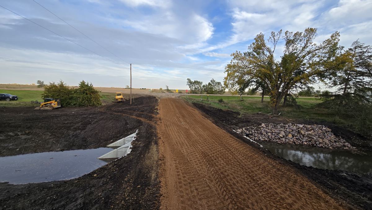 Gravel road rebuilt over a new culvert, with riprap at the outlet