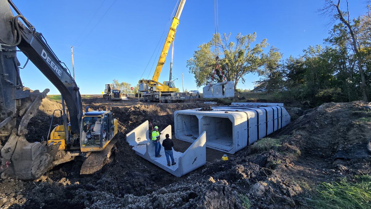 Excavator and crane setting precast concrete box culvert sections