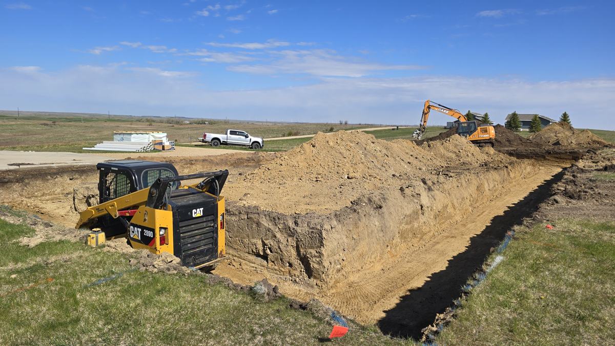 Skid steer and excavator digging a long trench